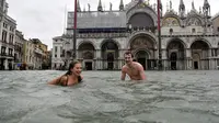 Sepasang wanita dan pria berenang di Lapangan Santo Marco yang terendam banjir air pasang di Venesia (AP/Luigi Constantini)