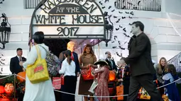 Presiden AS, Donald Trump didampingi Melania Trump membagikan permen kepada anak-anak saat open house perayaan pesta Halloween di Gedung Putih, Senin (30/10). Selain ratusan siswa, keluarga militer juga hadir di acara itu. (AP/Pablo Martinez Monsivais)
