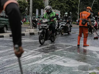 Sejumlah pengendara motor berkendara dengan hati-hati saat anggota Penanganan Prasarana dan Sarana Umum (PPSU) membersihkan tumpahan oli di kawasan Jalan Thamrin, Jakarta, Selasa (4/10/2022). Pembersihan ceceran tumpahan oli tersebut agar pengendara motor tidak terjatuh. (Liputan6.com/Faizal Fanani)