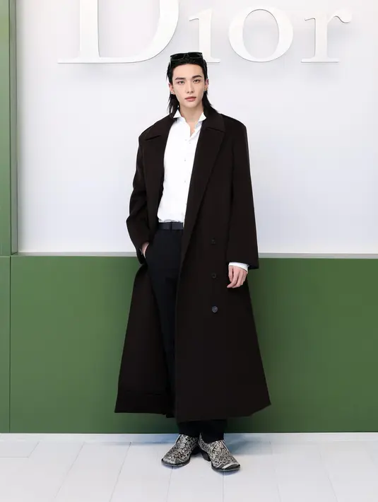 Hyunjin Stray Kids hadir dengan gaya formal modern mengenakan mantel wol hitam, kemeja katun putih berkerah wing collar, serta celana wol hitam. Ia menambahkan sabuk kulit hitam “Medaillon” dan sepatu derby hitam putih D de Dior yang memberikan sentuhan maskulin elegan. [Image Credit: Getty Images/DIOR]