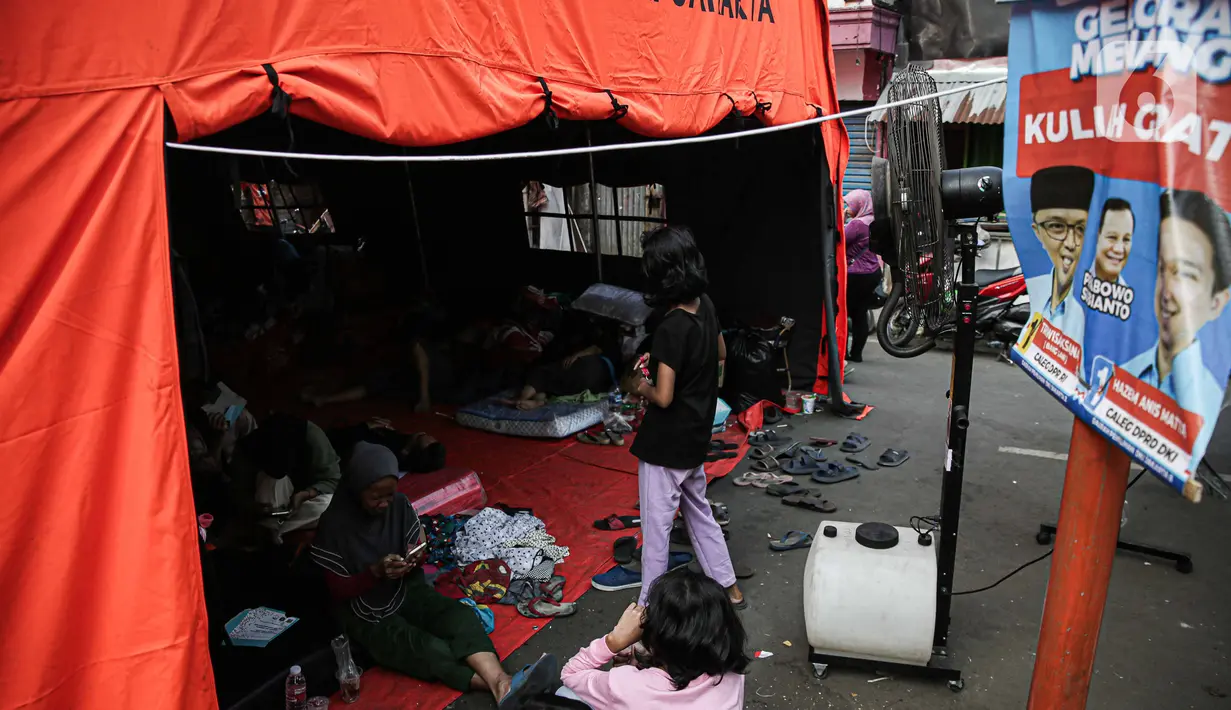 Warga korban kebakaran terlihat beristirahat dekat banner calon anggota legislatif (caleg) di Jalan Manggarai II, Tebet, Jakarta Selatan, Minggu (17/12/2023). (Liputan6.com/Faizal Fanani)