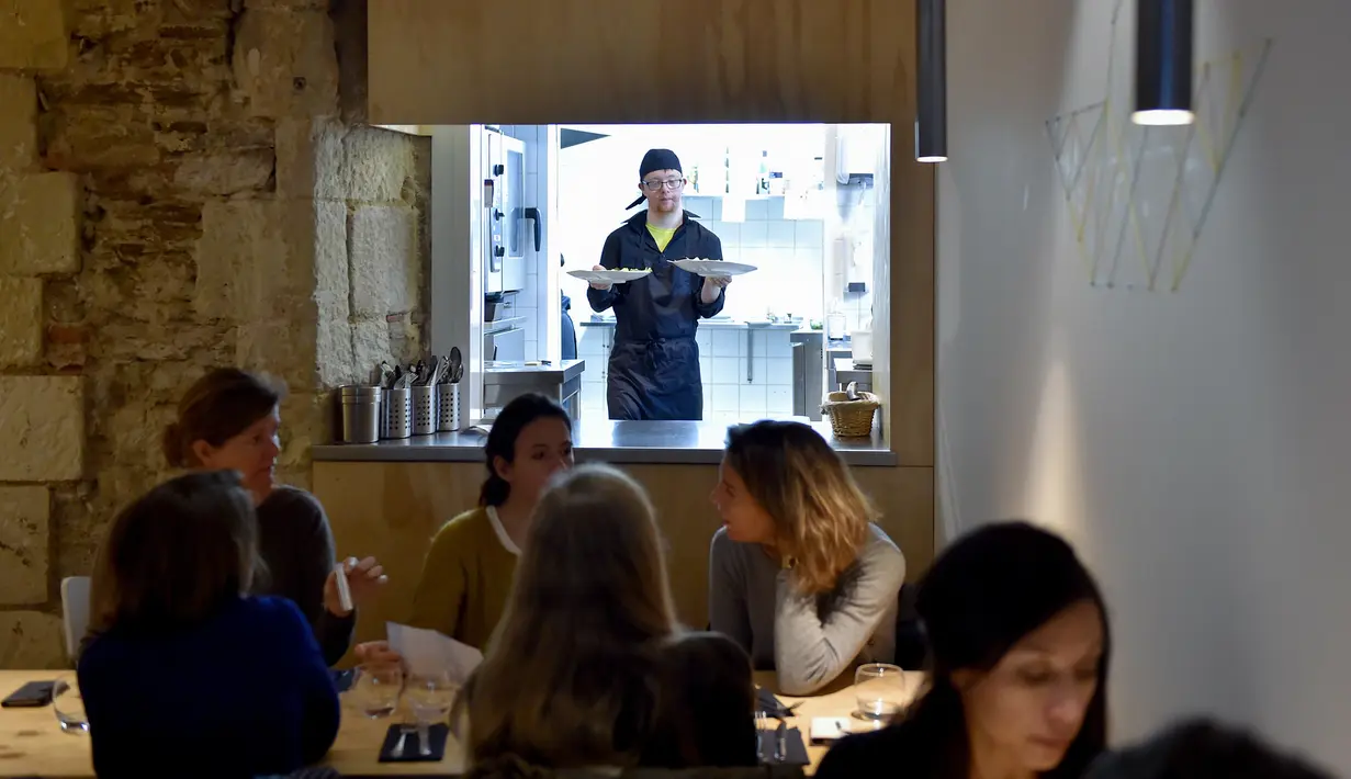 Asisten memasak dengan down syndrome memegang piring berisi menu makanan di restoran "Le Reflet" di Nantes, Prancis Barat, 9 Februari 2017. Lelievre (26), mempekerjakan sejumlah karyawan yang memiliki down syndrome di restorannya. (LOIC VENANCE/AFP)