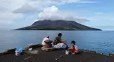 Orang-orang memancing di pelabuhan di pulau Tagulandang di Sitaro, Sulawesi Utara dengan latar belakang gunung berapi Ruang yang mengeluarkan asap, Jumat (19/4/2024). (Ronny Adolof BUOL / AFP)