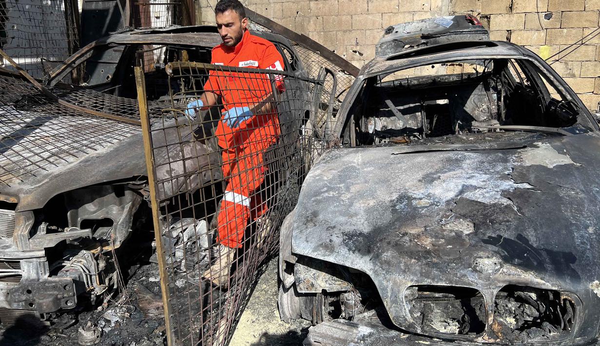 Seorang petugas medis berdiri di samping puing-puing mobil di kamp pengungsi Palestina Ain al-Hilweh, dekat Sidon di selatan Lebanon, pada Rabu 19 November 2025. Sebuah serangan udara Israel menghantam kamp pengungsi Palestina Ain al-Hilweh di Lebanon selatan. (Mahmoud ZAYYAT/AFP)