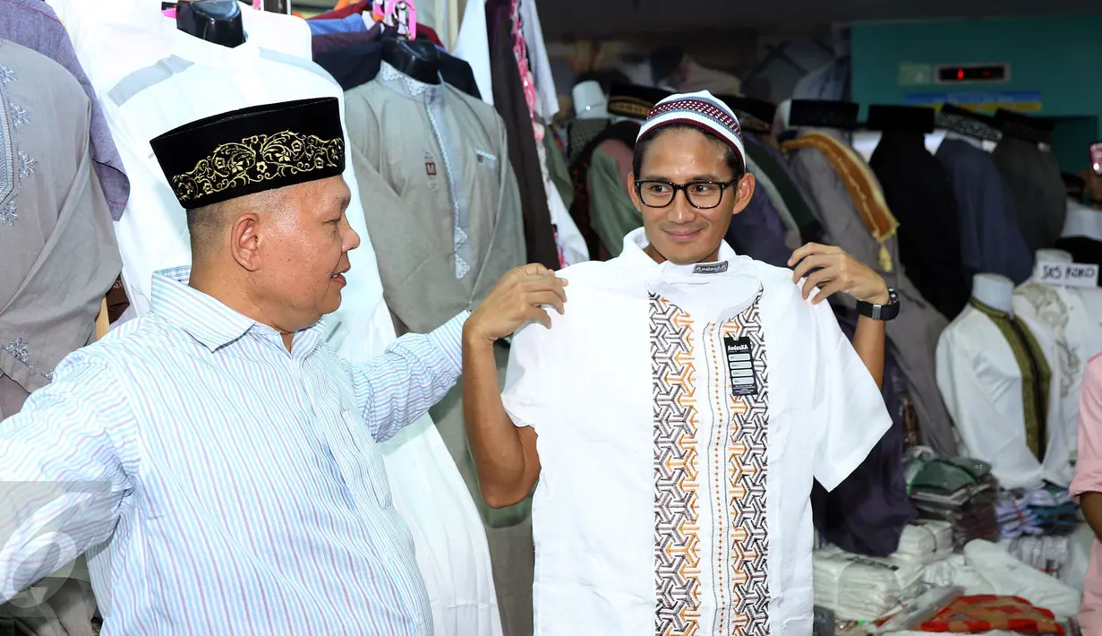 Cawagub DKI Jakarta, Sandiaga S Uno (kanan) mencoba pakaian muslim saat sosialisasi di pasar Blok A dan B Tanah Abang, Jakarta, Senin (26/12). Dihadapan para pedagang, Sandi mensosialisasikan beberapa program andalannya. (Liputan6.com/Helmi Fithriansyah)