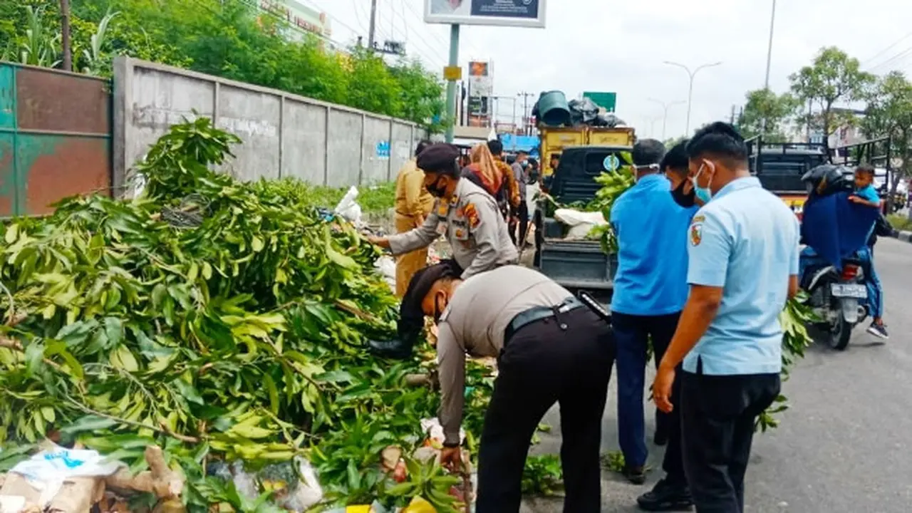 Personel Polsek Tampan Pekanbaru mengangkut tumpukan sampah di sebuah ruas jalan.