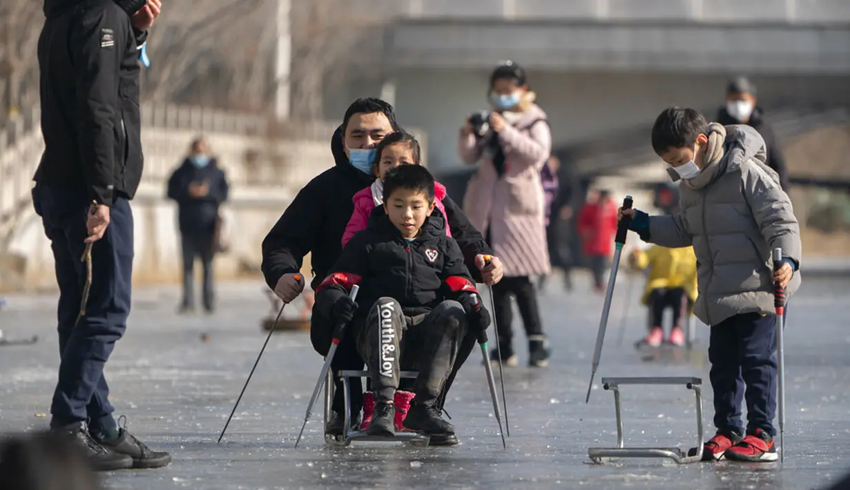 Orang-orang yang memakai masker wajah untuk melindungi dari penyebaran virus corona COVID-19 menggunakan kursi untuk meluncur melintasi permukaan kanal yang membeku di Beijing, China, Sabtu (30/1/2021). (AP Photo/Mark Schiefelbein)