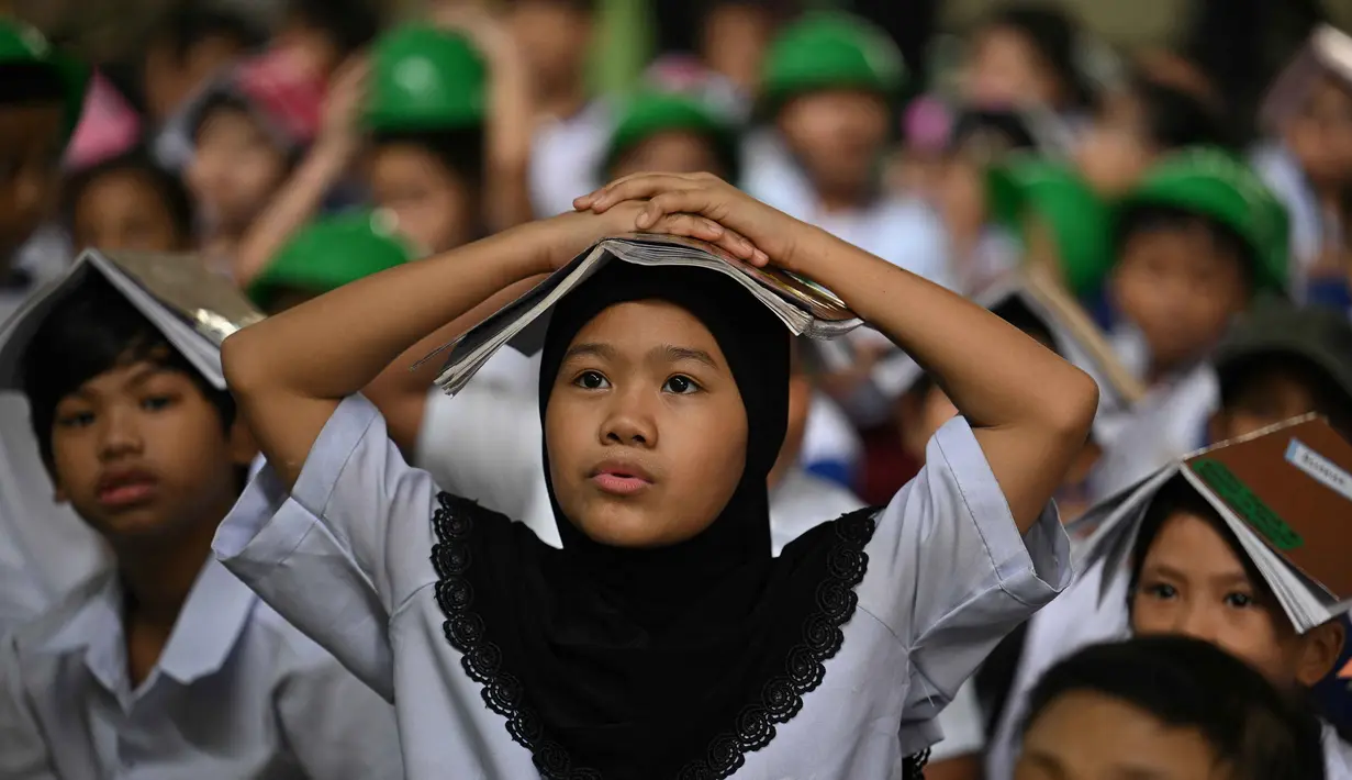 Para pelajar muda meletakkan buku di kepala mereka saat berkumpul di pusat evakuasi yang telah ditentukan di luar gedung sekolah selama latihan gempa bumi di salah satu sekolah dasar di Manila, Filipina pada 11 September 2025. (Ted ALJIBE/AFP)