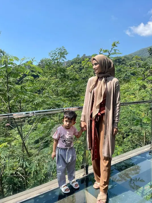 Nadya tampil dengan pakaian bernuansa earth tone dari kerudung hingga celananya. Si kecil tampil dengan kaos pink dan celana abu-abunya. [@nadyamustikarahayu]