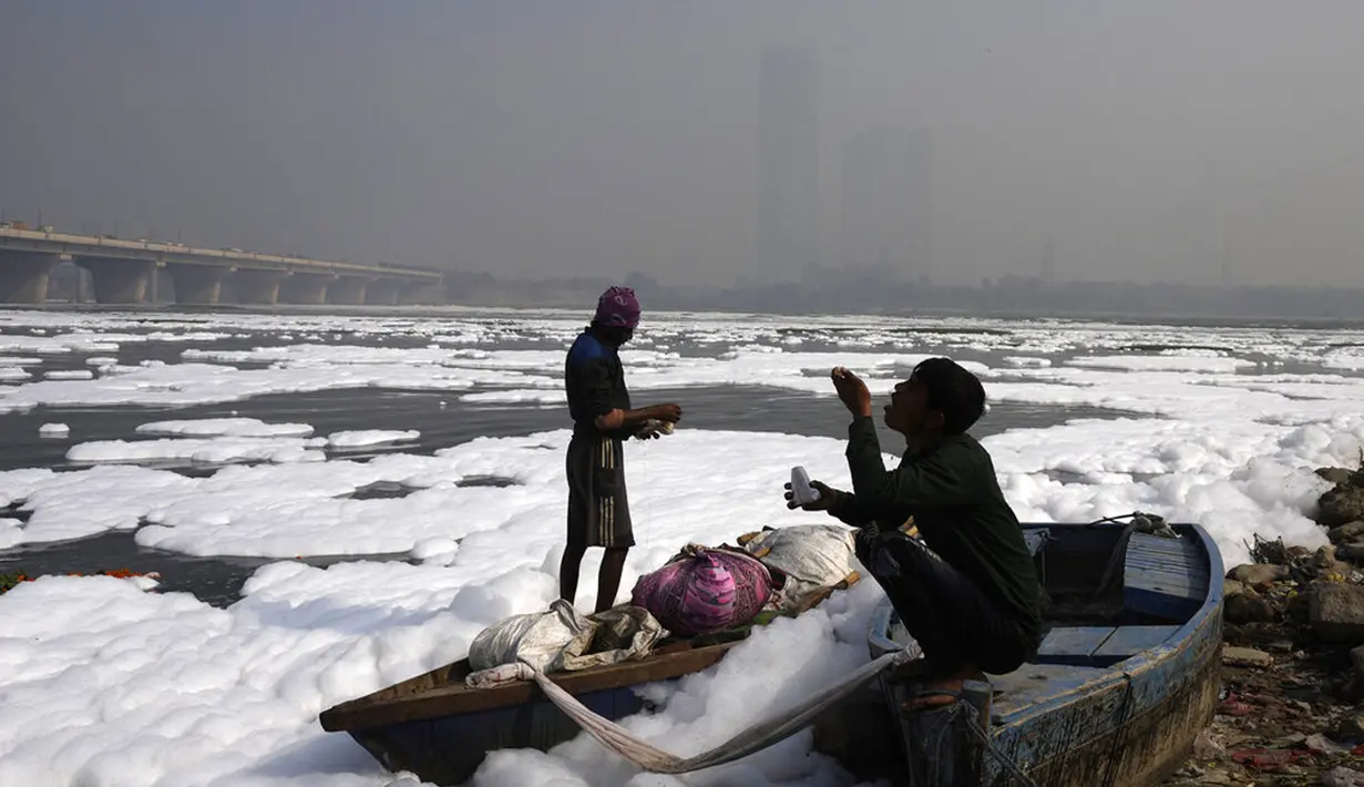 Seseorang makan makanan ringan sambil duduk di perahunya di Sungai Yamuna yang tertutup busa kimia karena polusi industri dan domestik saat cakrawala diselimuti kabut asap beracun, New Delhi, India, 17 November 2021. New Delhi merupakan kota yang kerap diselimuti kabut asap. (AP Photo/Manish Swarup)