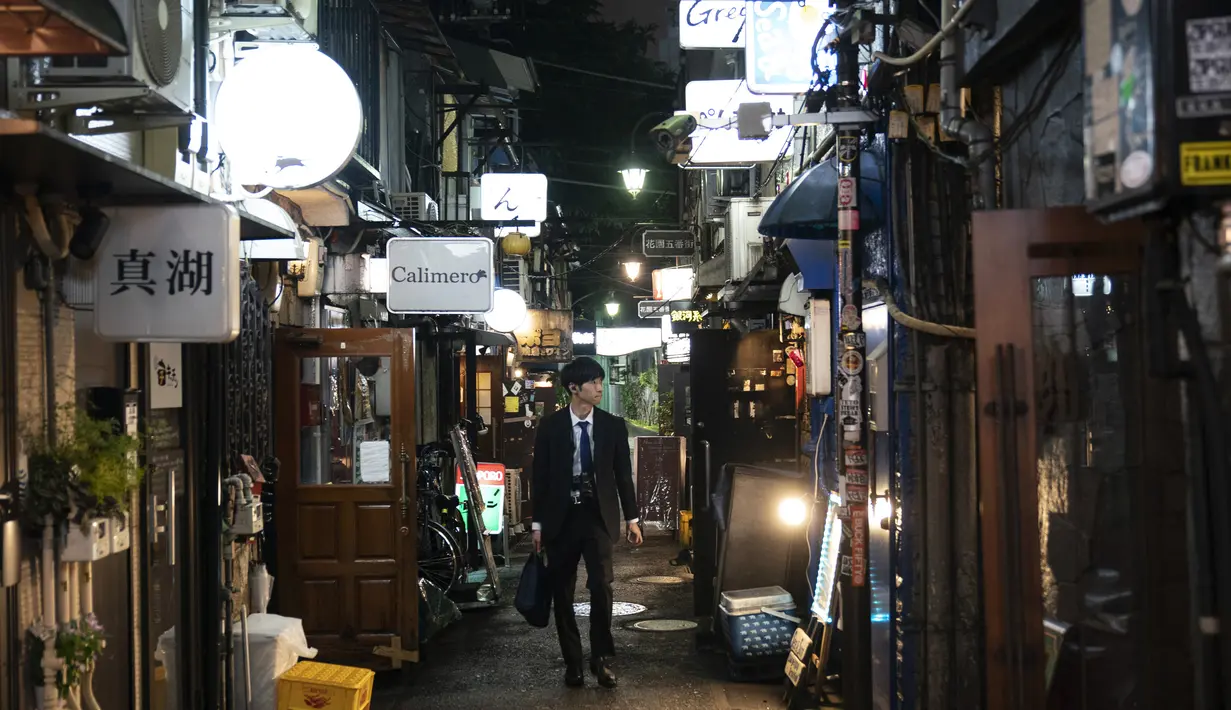Seorang pria berjalan melalui gang sempit yang dikelilingi bar dan restoran kecil di Golden Gai di distrik Shinjuku, Tokyo (17/7/2019). Gang-gang di kawasan ini merupakan jalan pribadi, bukan jalan umum. (AP Photo / Jae C. Hong)