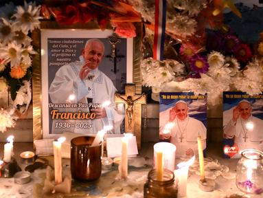 Lilin dan bunga diletakkan di samping foto mendiang Paus Fransiskus di pintu masuk Katedral Buenos Aires, Argentina pada tanggal 21 April 2025. (Luis ROBAYO/AFP)