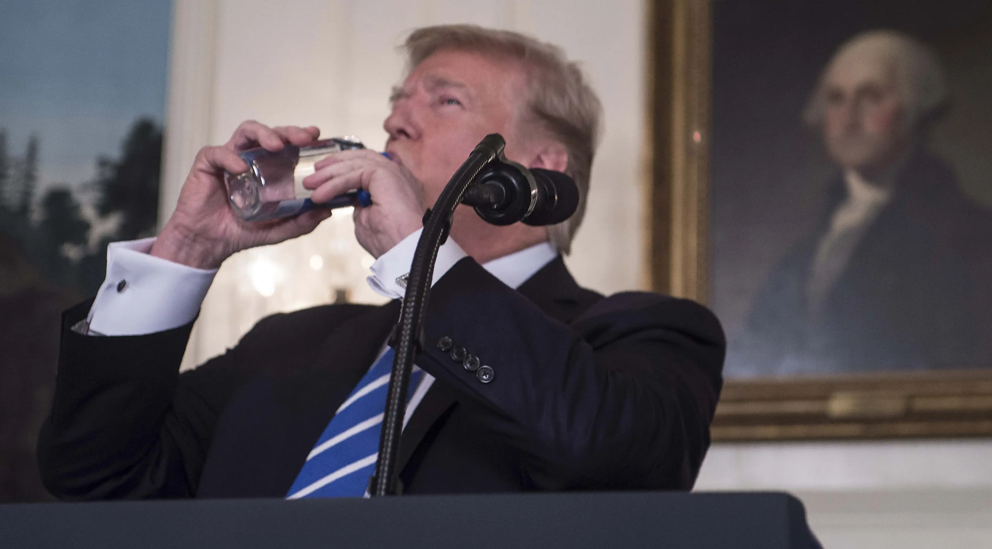 Presiden AS, Donald Trump meminum botol air mineral disela menyampaikan pidato di Ruang Diplomatik Gedung Putih, Rabu (15/11). Sementara itu warganet justru mengkritik Trump yang meminum air mineral impor merek Fiji Water. (MARK WILSON/GETTY IMAGES/AFP)
