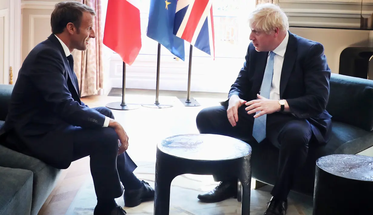 Presiden Prancis Emmanuel Macron berbincang dengan PM Inggris, Boris Johnson dalam kunjungan kenegaraan di Istana Elysee, Paris, Kamis (22/8/2019). Dalam pertemuan, Johnson tertangkap kamera bercanda ke arah kamera dan meletakkan kakinya di meja kopi. (Christophe Petit Tesson, Pool via AP)