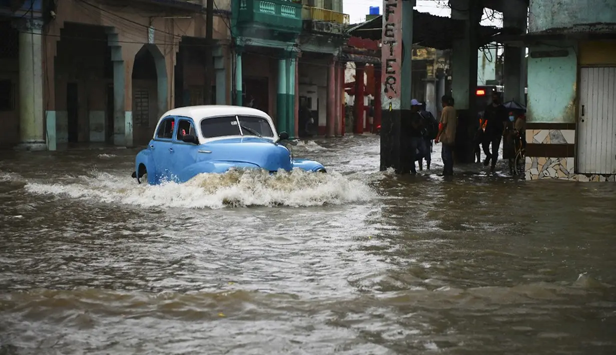 Sebuah mobil tua Amerika Serikat melewati jalan yang banjir di Havana, Kuba, 30 Juni 2021. Hujan deras dan selokan yang tidak berfungsi menyebabkan banjir di jalan-jalan di Havana. (YAMIL LAGE/AFP)