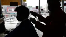 Tukang cukur mengenakan alat pelindung diri (APD) saat memotong rambut pelanggan di sebuah tempat pangkas rambut di Manila, 8 Juni 2020. Filipina mengizinkan barbershop dan salon kecantikan beroperasi kembali dengan menerapkan langkah-langkah ketat pencegahan pandemi Covid-19. (AP/Aaron Favila)