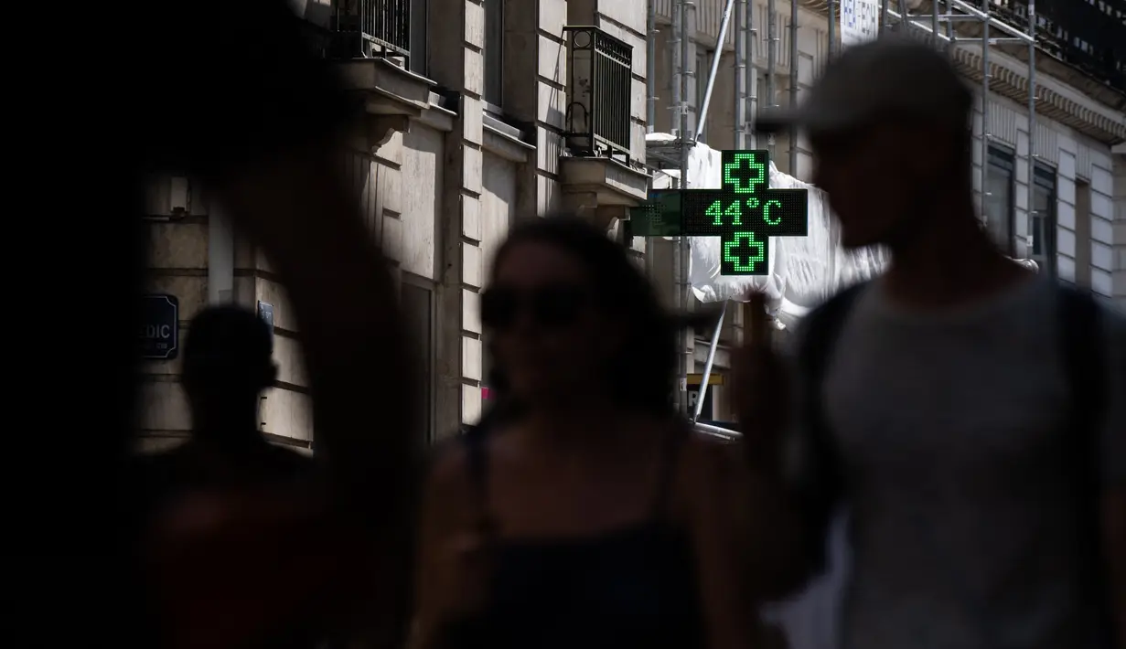 <p>Pejalan kaki berjalan menyusuri jalan saat lampu apotek menunjukkan suhu turun 44 derajat celsius di Nantes, Senin (18/7/2022). Peramal cuaca menempatkan 15 departemen di sebagian besar sisi barat Prancis ke status siaga tertinggi untuk suhu ekstrem saat gelombang panas melanda negara itu dan akan mencapai puncaknya. (Loic VENANCE / AFP)</p>