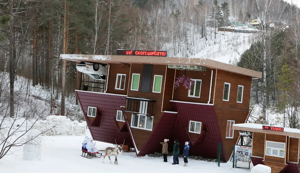 Seorang pekerja berpakaian seperti Ded Moroz atau Santa Claus dari Rusia bersama cucunya Snegurochka duduk di kereta Rusa menyambut pengunjung rumah terbalik Royev Ruchey Park, Krasnoyarsk, Rusia (7/12). (Reuters/Ilya Naymushin)