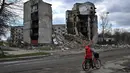 Seorang pria membawa sepedanya melewati gedung-gedung yang hancur di kota Borodianka, barat laut Kiev pada 4 April 2022. Saat pasukan Rusia mundur, kota kecil Borodianka, 50 km barat laut Kiev, menjadi reruntuhan. (Sergei SUPINSKY / AFP)