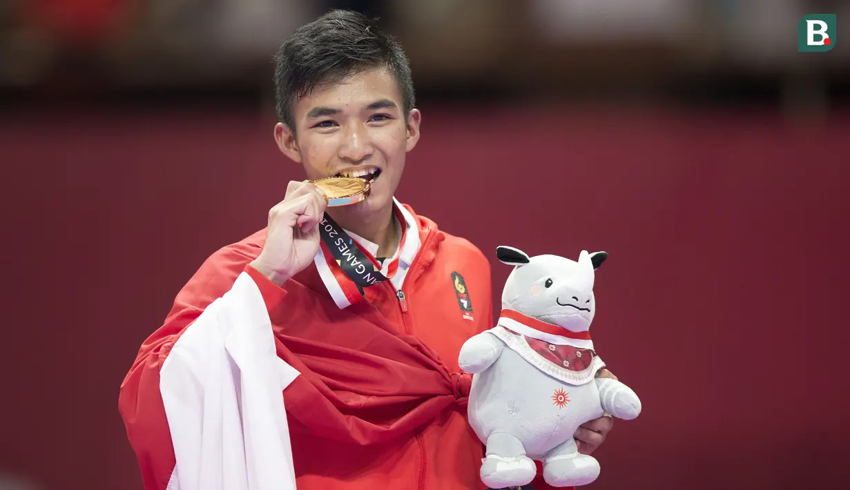 Karateka Indonesia, Rifki Ardiansyah Arrosyiid, menggigit medali usai beraksi pada Asian Games di JCC Senayan, Jakarta, Minggu (26/8/2018). Rifki berhasil medapat medali emas di nomor kumite 60 kilogram. (Bola.com/Peksi Cahyo)