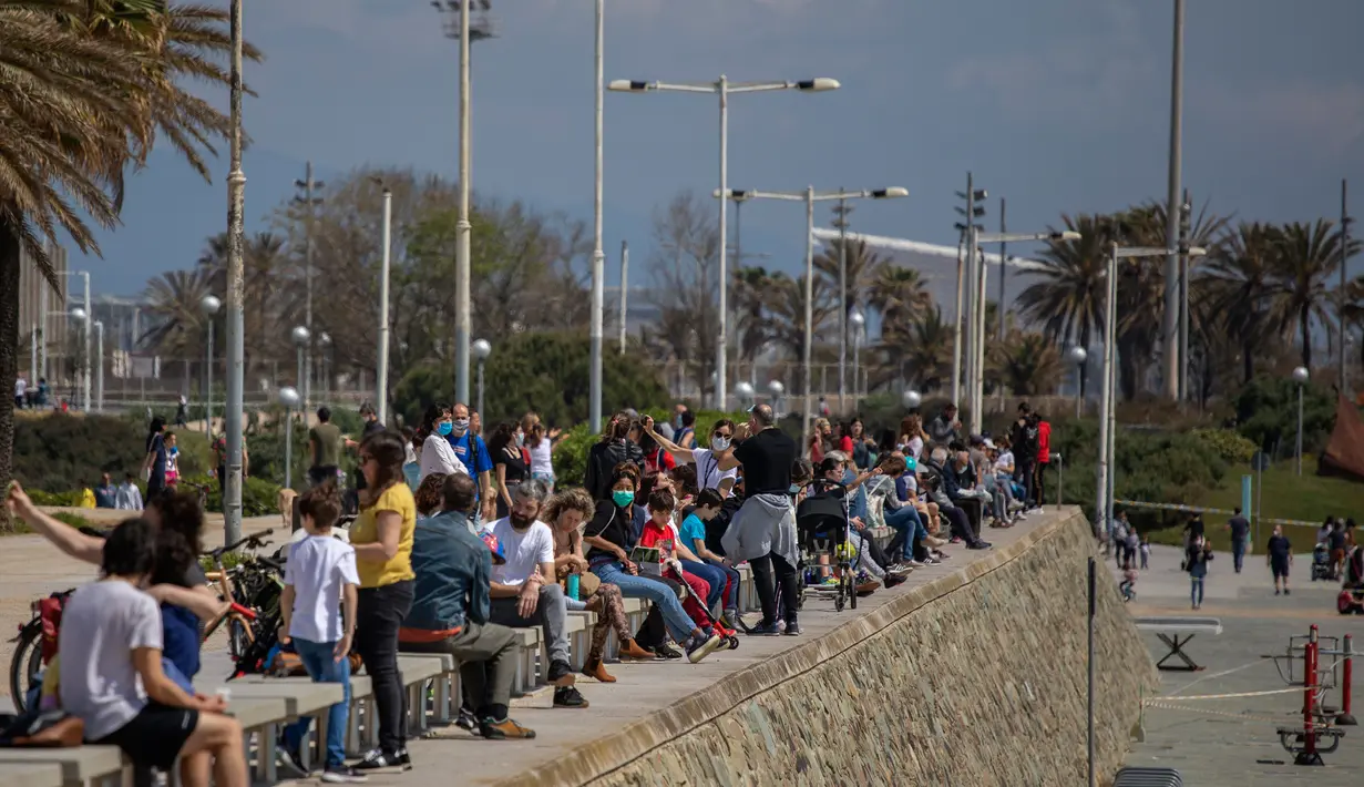 Keluarga dengan anak-anak mereka duduk di bulevar ketika polisi berpatroli di pantai, di mana aksesnya dilarang, di Barcelona, Spanyol (26/4/2020). Merasa sudah melewati puncak epidemi COVID-19, pelonggaran dilakukan secara bertahap.  (AP Photo/Emilio Morenatti)