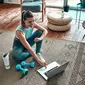 Seorang wanita sporty dalam pakaian olahraga sedang duduk di lantai dengan dumbel dan protein shake atau sebotol air dan menggunakan laptop di rumah di ruang tamu. Konsep olahraga dan rekreasi/Shutterstock-ORION PRODUCTION.