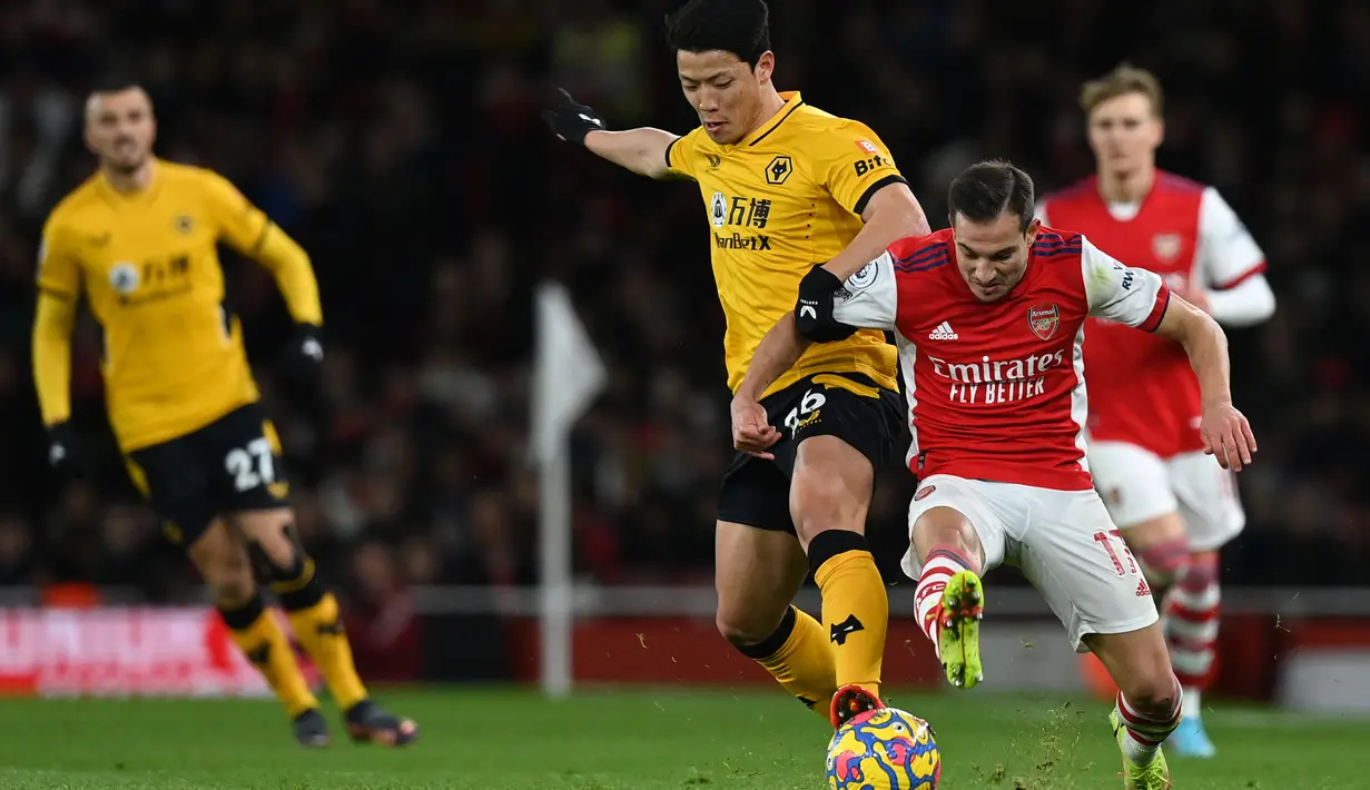 Striker Wolverhampton Wanderers Hwang Hee-chan (tengah) berebut bola dengan bek Arsenal Cedric Soares pada partai tunda pekan ke-20 Liga Inggris di Emirates Stadium, Jumat (25/2/2022) dini hari WIB. Arsenal menang dramatis 2-1 berkat dua gol di menit akhir. (Glyn KIRK / AFP)