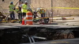 Sejumlah petugas bekerja di dekat lubang besar (sinkhole) di wilayah Brooklyn, New York, Selasa (4/8/2015). Lubang yang terbentuk di persimpangan pemukiman Sunset Park itu disebabkan erosi dan merusak pipa air serta aspal jalan. (AFP/Kena Betancur)