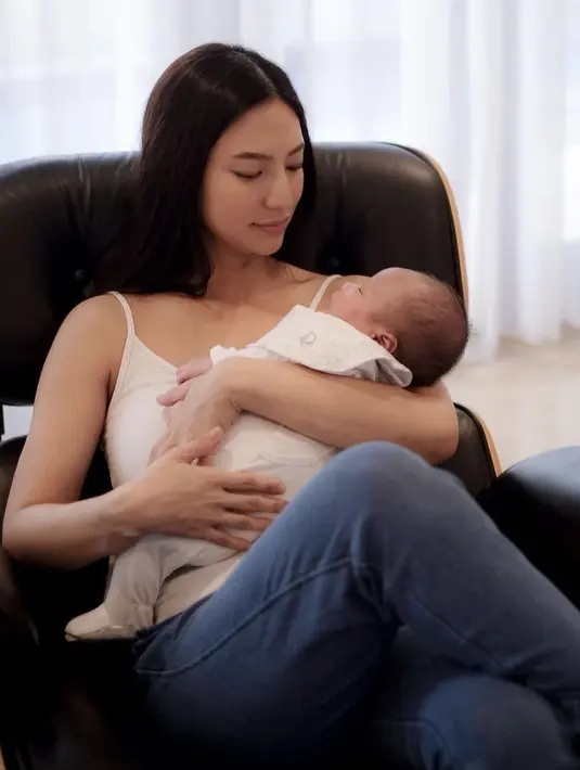 <p>Duduk di sofa hitam, Nadia Saphira terlihat menggendong sang anak. Ia tampil dengan tank top putih dipadukan celana denim. (@nadsap)</p>