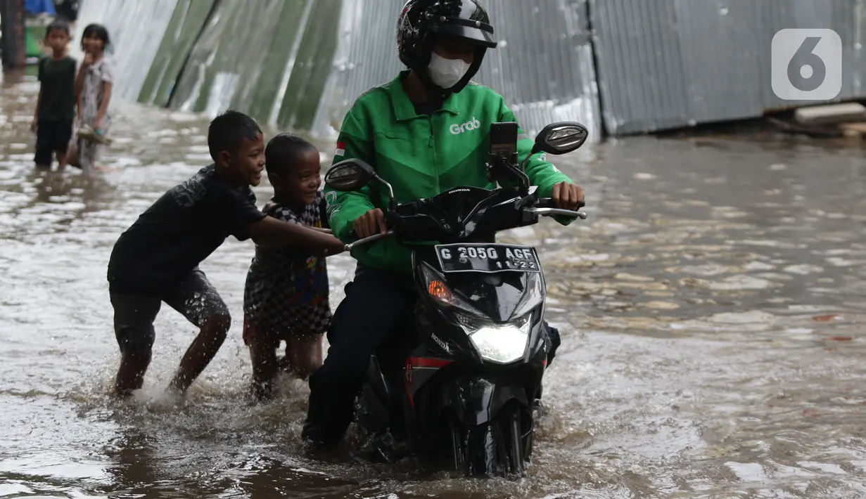 Anak-anak mendorong motor pengemudi ojol melewati sebagian Jalan Bungur Besar Raya yang tergenang air, Jakarta, Selasa (18/1/2022). Genangan air membuat arus lalu lintas di sekitar depan PN Jakarta Pusat menjadi terganggu dan tersendat. (Liputan6.com/Helmi Fithriansyah)