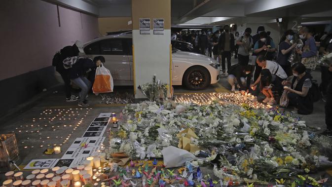 Para pengunjuk rasa menyalakan lilin di dekat bunga-bunga di lokasi tempat mahasiswa Alex Chow Tsz-lok jatuh di Hong Kong (8/11/2019). Chow ditemukan terbaring dengan genangan darah di sebuah tempat parkir mobil, yang menjadi sasaran penembakan gas air mata oleh polisi. (AP Photo/Kin Cheung)