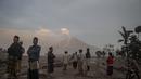 Orang-orang berdiri di depan Gunung Semeru menyusul letusan gunung berapi di desa Kajar Kuning di Lumajang (5/12/2022). Gunung Semeru meletus pada tanggal 4 Desember memuntahkan awan abu panas setinggi satu mil dan sungai lava di sisinya sambil memicu evakuasi hampir 2.000 orang tepat satu tahun setelah letusan besar terakhirnya menewaskan puluhan orang. (AFP/Juni Kriswanto)