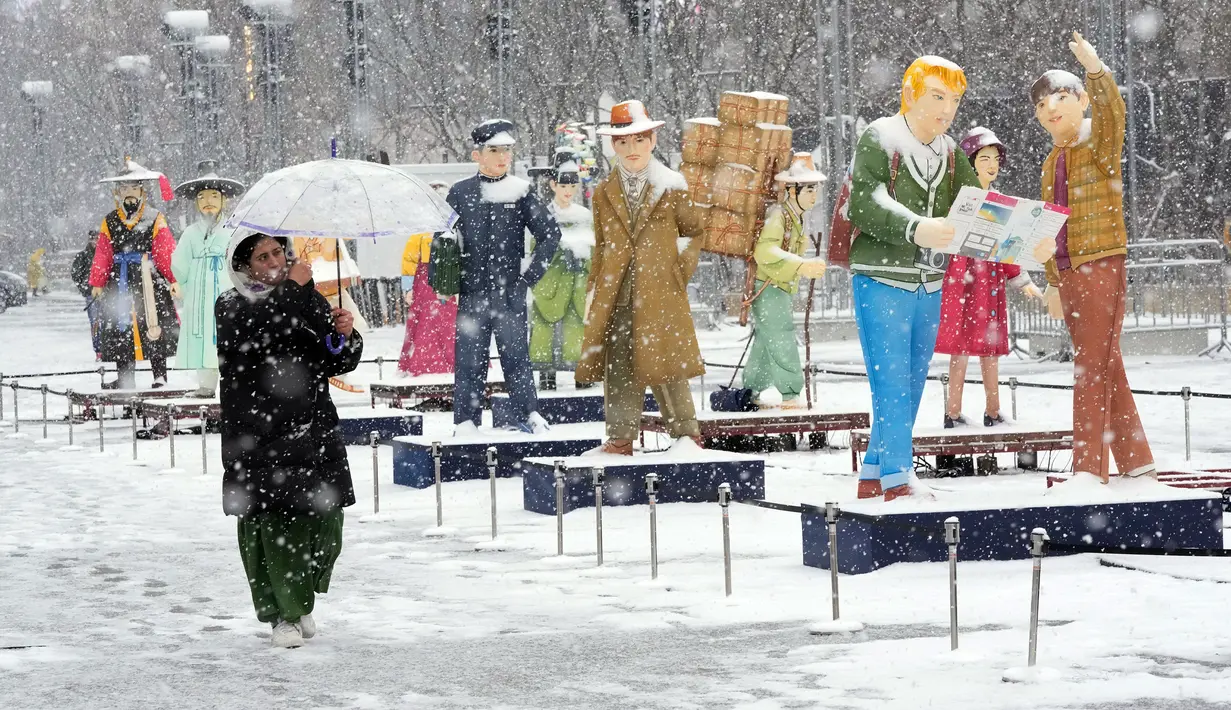 Seorang wanita berjalan saat turun salju di samping lentera di Gwanghwamun Square, Seoul, Korea Selatan, 15 Desember 2022. (AP Photo/Ahn Young-joon)