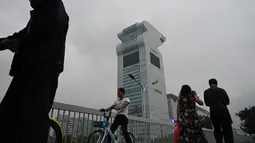 Orang-orang melewati gedung pencakar langit Pangu Plaza di seberang Stadion Olimpiade Bird's Nest, Beijing, Selasa (20/7/2019). Gedung yang pernah masuk dalam film Transformers: Age of Extinction itu terjual dalam lelang online dengan harga 734 juta USD atau sekitar Rp10,5 triliun. (GREG BAKER/AFP)