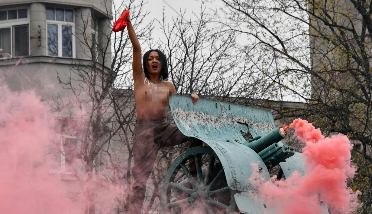 Seorang aktivis wanita gerakan hak perempuan Femen meneriakkan slogan-slogan di tiang monumen Soviet di pusat kota Kiev, Ukraina (7/11). Aktivis tersebut menggelar aksi memperingati 100 tahun Revolusi Bolshevik. (AFP Photo/Genya Savilov)