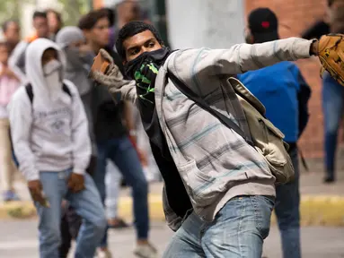 Mahasiswa Venezuela Central University melempar batu ke arah polisi selama protes menuntut peningkatan anggaran beasiswa dan membuka kembali kafetaria universitas di Caracas, Venezuela (21/11). (AP Photo/Ariana Cubillos)