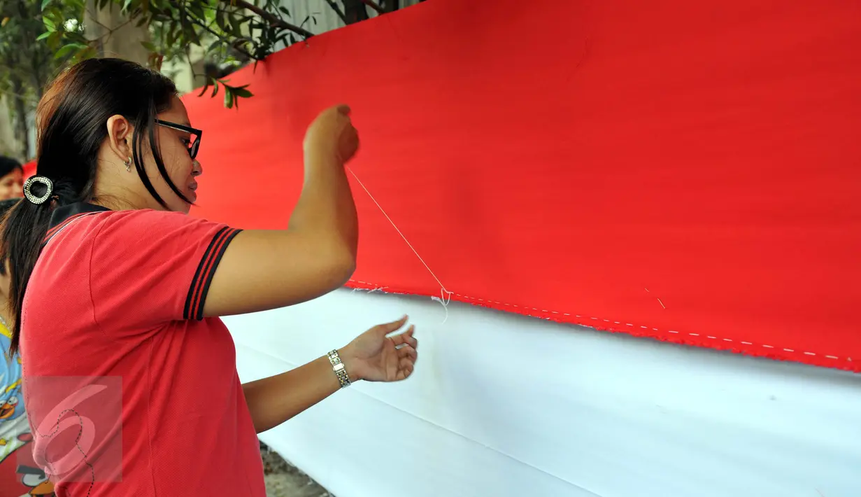 Seorang warga terlihat serius menjahit bendera merah putih saat mengikuti lomba di Kelurahan Pekojan, Jakarta, Minggu (16/8/2015). Lomba memperebutkan trofi lurah dan sejumlah uang. (Liputan6.com/Panji Diksana)