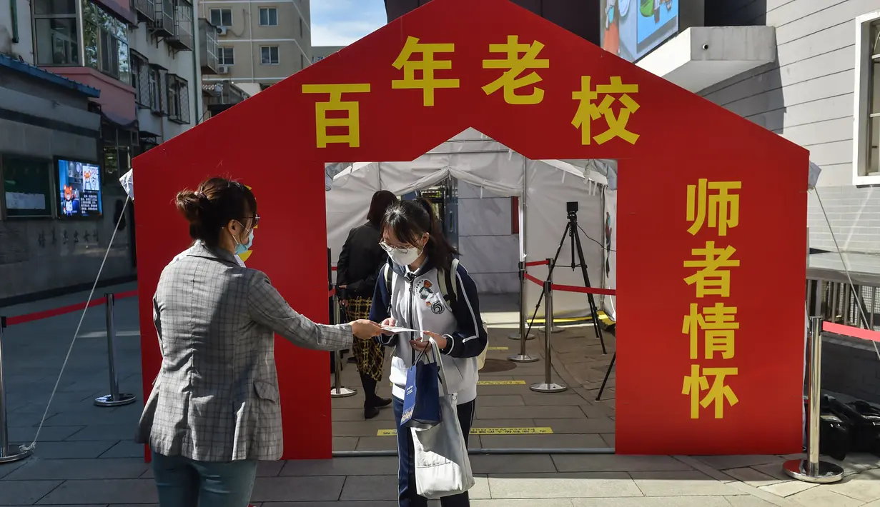 Seorang guru menyerahkan brosur tentang langkah pencegahan dan pengendalian wabah COVID-19 kepada seorang siswa yang hendak memasuki gedung Sekolah Menengah No. 166 di Beijing, ibu kota China, (11/5/2020). (Xinhua/Peng Ziyang)