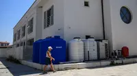 Seorang perempuan melewati tangki air holtel di provinsi Izmir, Turki barat, pada 31 Juli 2025. Pemerintah daerah di Cesme, sebuah resor tepi laut populer di provinsi Izmir di pesisir barat Turki&mdash;harus memutus pasokan air minum selama 10 jam sehari akibat kekeringan. (Yasin AKGUL/AFP)
