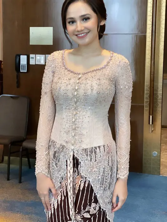 Syifa Hadju tampil memesona dengan heart neckline kebaya krem dengan detail kancing bungkus di bagian depan. Dipadukan dengan kain untuk bawahannya. Sanggul minimalis dengan makeup natural pun membuat Syifa semakin cantik. Dok. Instagram @guginugraha