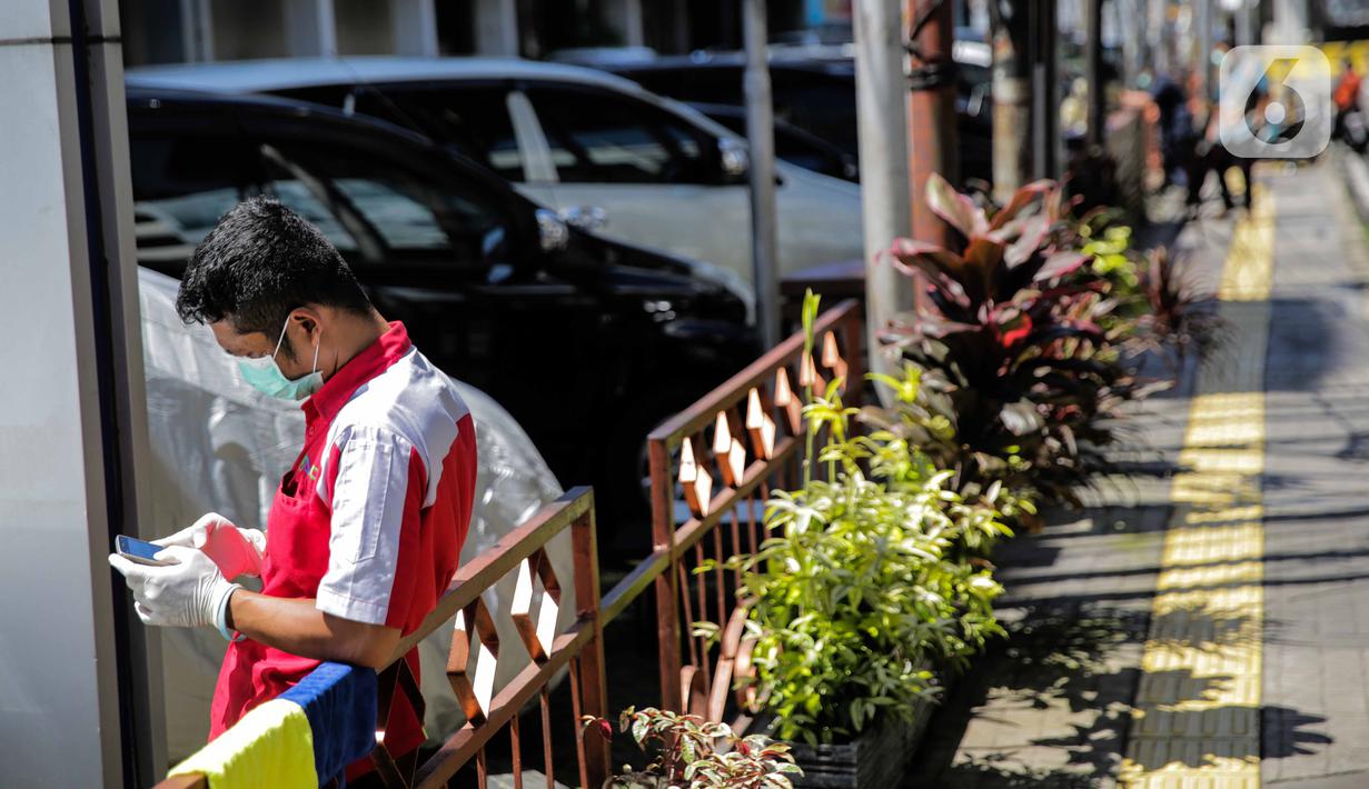 Seorang pegawai bermain ponsel sambil berjemur di bawah sinar matahari di Kawasan Fatmawati, Jakarta, Selasa (31/3/2020). Berjemur diri di bawah sinar matahari saat pagi merupakan salah satu upaya yang paling sederhana untuk menjaga kesehatan selama wabah virus COVID-19. (Liputan6.com/Faizal Fanani)