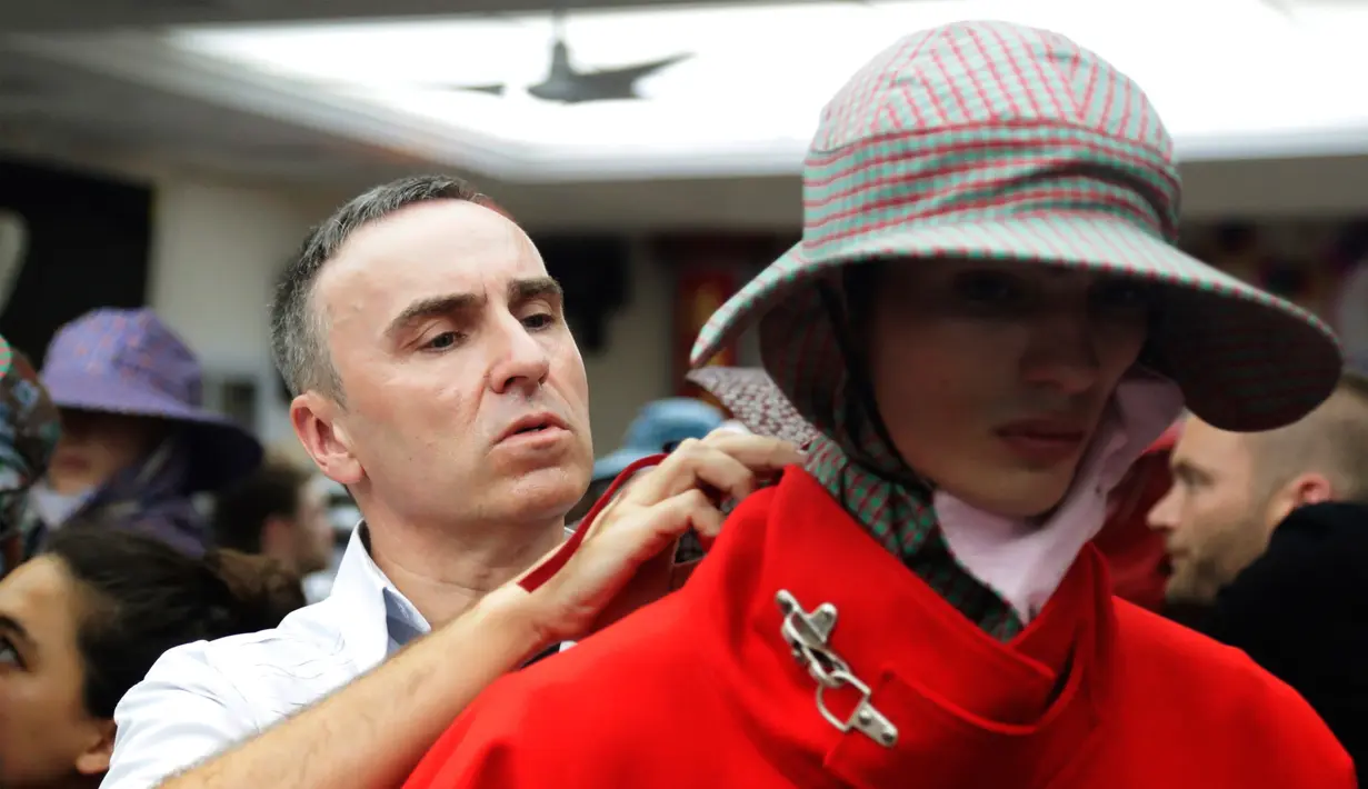 Perancang busana Raf Simons (kiri) mengatur kembali pakaian yang diekanakan model sebelum peragaan dimulai di Men’s Fashion Week (11/7). Rancangan Raf tidak hanya untuk satu gender, tetapi bisa juga dipakai oleh semua gender. (AP/Frank Franklin)