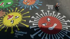 Pengendara motor melewati melewati grafiti virus corona yang dilukis di jalan selama penerapan lockdown nasional di Chennai, India, Senin (13/4/2020). Grafiti itu dibuat untuk meningkatkan kesadaran warga yang keluyuran keluar rumah saat lockdown karena pandemi virus corona. (Arun SANKAR/AFP)