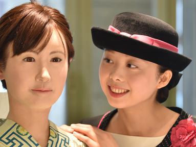 Seorang pengunjung berpose bersama robot humanoid ChihiraAico (kiri) yang mengenakan kimono Jepang di Tokyo pada 20 April 2015. Robot ini bisa tersenyum, menyanyi dan memberikan bimbingan pada pengunjung. (AFP PHOTO/KAZUHIRO)