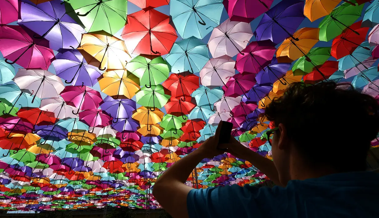 Pengunjung mengambil gambar instalasi Umbrella Sky Project di Aix-en-Provence, Prancis, Jumat (28/6/2019). Spot berteduh yang instagramable tersebut merupakan karya seniman Portugis Patricia Cunha. (BORIS HORVAT/AFP)