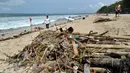 Turis berjalan di sepanjang pantai Kuta melintasi puing-puing dan sampah di Bali, Minggu (9/12). Kawasan pantai Kuta kembali dipenuhi oleh sampah hanyut terbawa oleh gelombang. (SONNY TUMBELAKA / AFP)