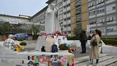 Orang-orang berdiri di depan patung Yohanes Paulus II di luar Rumah Sakit Universitas Gemelli tempat Paus Fransiskus dirawat karena pneumonia, di Roma pada 8 Maret 2025. (ANDREAS SOLARO/AFP atau pemberi lisensi/AFP)