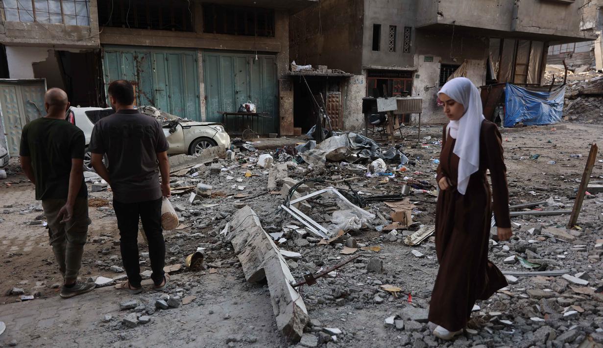 Seorang wanita Palestina berjalan melewati orang-orang yang memeriksa puing-puing bangunan tempat tinggal setelah serangan Israel di Kota Gaza pada Kamis 4 Juni 2026. (Omar AL-QATTAA/AFP)