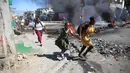 Seorang wanita dengan putrinya berjalan melewati barikade yang didirikan oleh anggota polisi saat mereka memprotes tata kelola polisi yang buruk di Port-au-Prince, Haiti, 26 Januari 2023. Banyak bisnis dan sekolah tutup setelah aksi protes. (AP Photo/Odelyn Joseph)