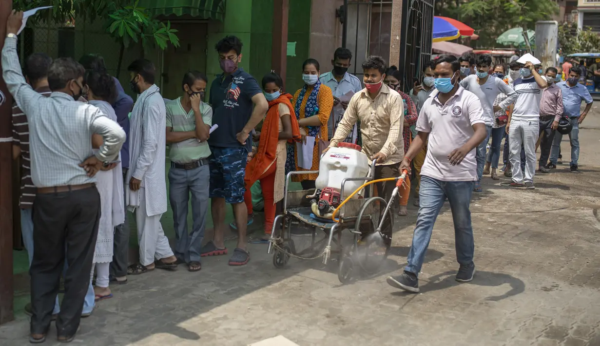 Petugas kesehatan membawa mesin sanitasi di kursi roda sambil membersihkan kompleks rumah sakit ketika orang-orang menunggu untuk tes COVID-19 di Noida, pinggiran New Delhi, India, Rabu (7/4/2021). India mencapai puncak baru dengan 115.736 kasus COVID-19 dalam 24 jam. (AP Photo/Altaf Qadri)